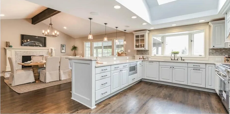 Remodeled open-plan kitchen with white shaker cabinets, stone countertops, a bay window over the sink, glass pendant lights and wide-plank hardwood floors
