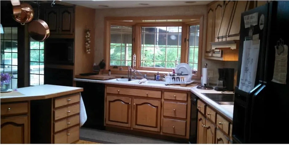 The same kitchen before remodeling, with dark oak raised-panel cabinets, laminate countertops and black appliances