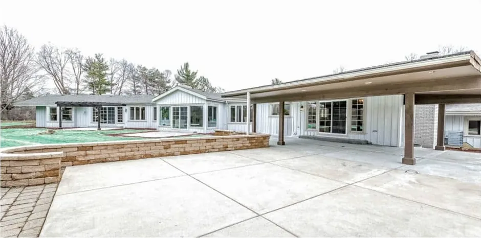 Finished rear exterior with a covered porch, white board-and-batten siding, a cut-stone seat wall and a wide poured-concrete patio