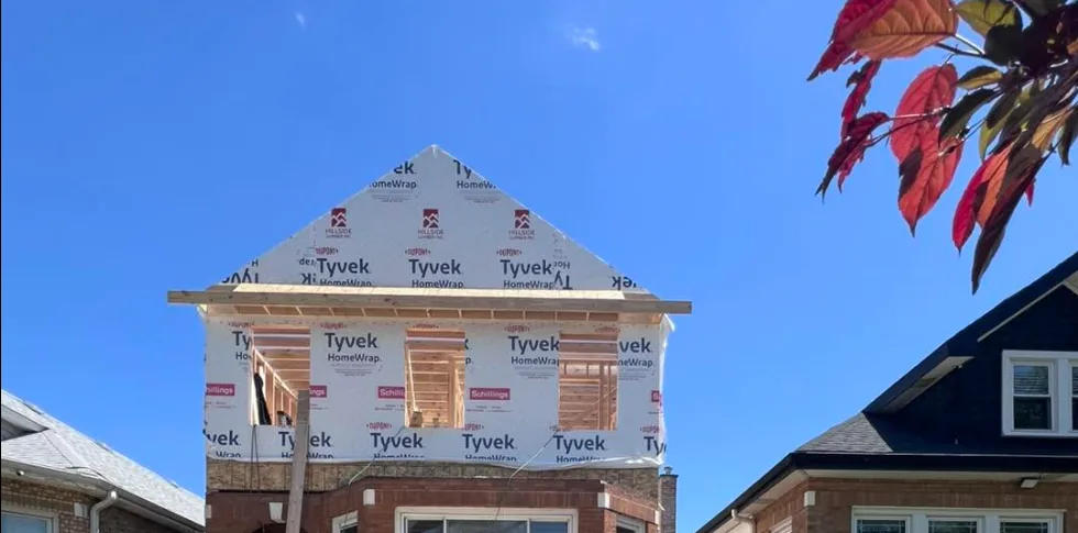 A second-floor addition framed and wrapped in house wrap above the brick first story of a Chicago-style home, with the new gable roofline in place